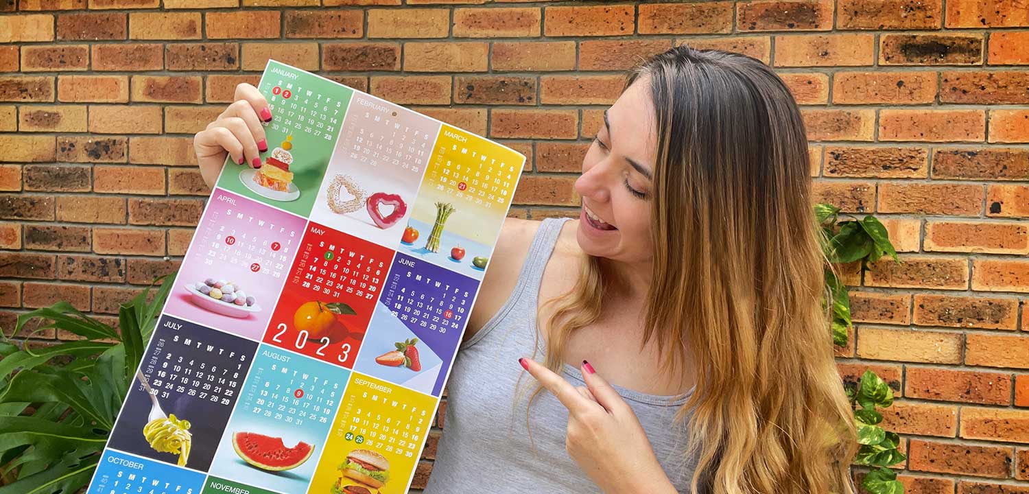 Annemarie Horne standing in the garden holding a colourful 2023 calendar